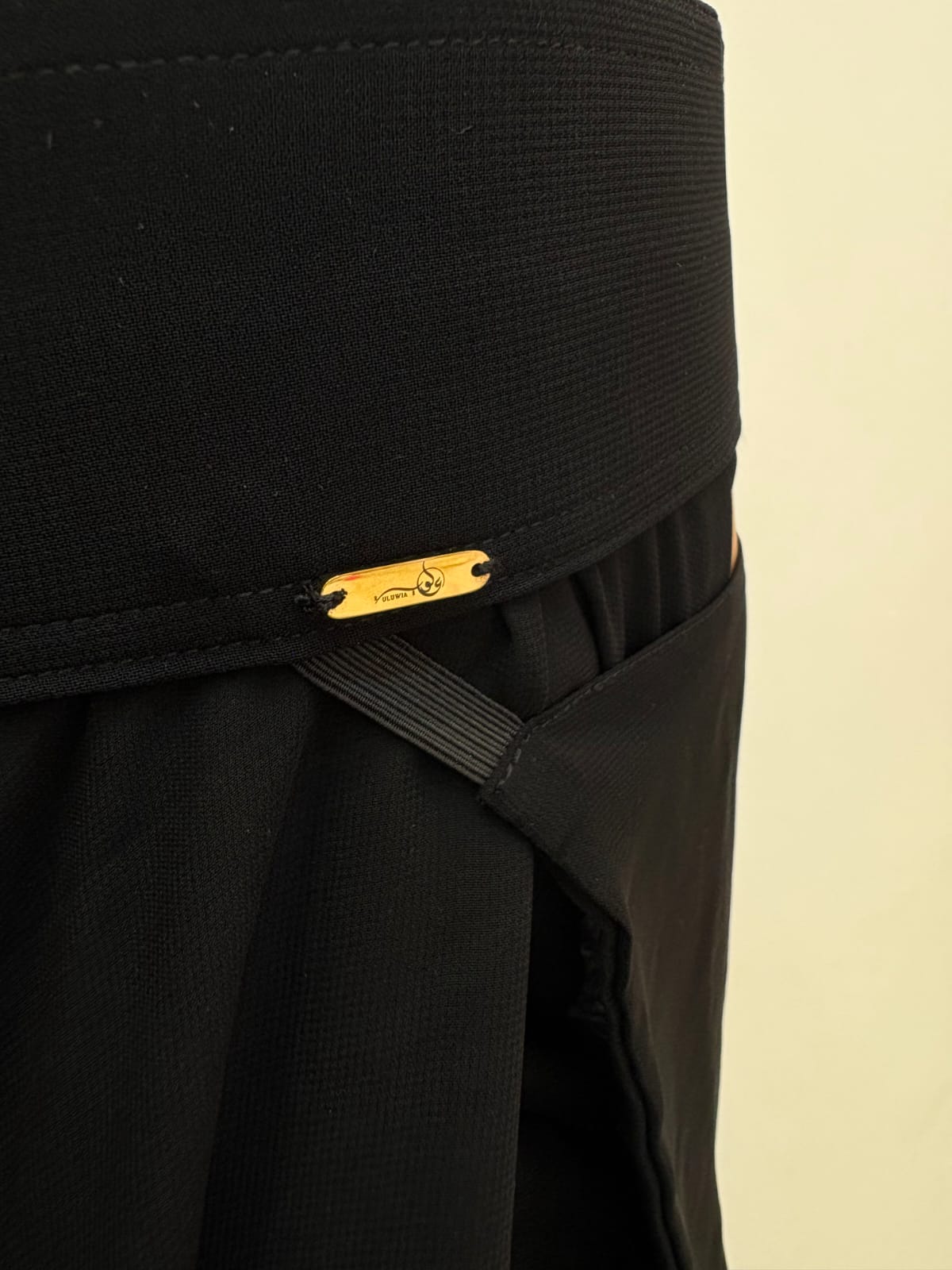 The gold Uluwia name plate stitched onto black fabric